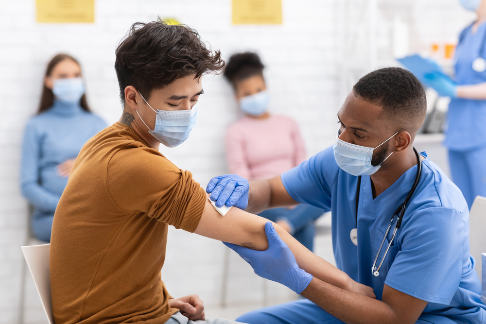 Patient receiving flu vaccine with others waiting to receive their vaccine in the background.