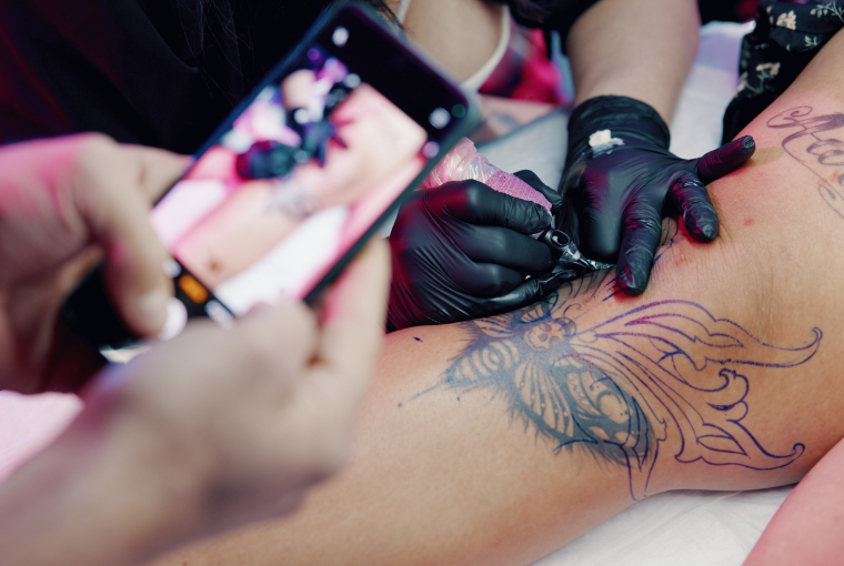 Someone films a tattoo on their mobile phone to use as UGC on Instagram while the artist inks their client