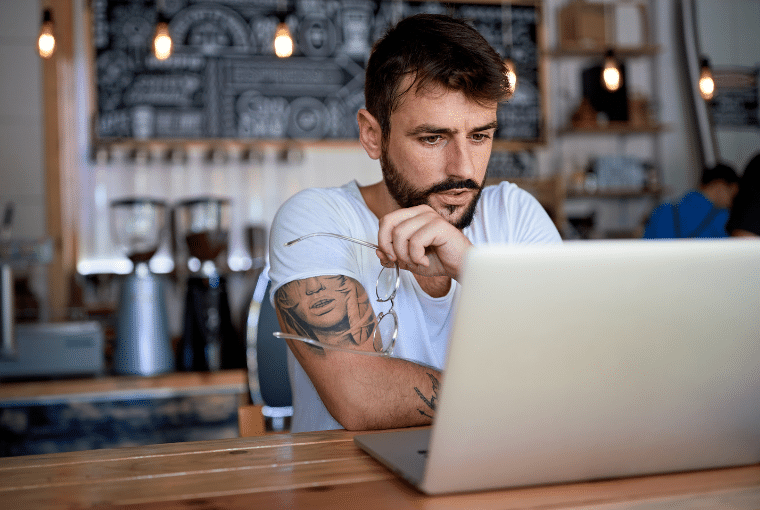 Tattoo professional on a coffee break looks thoughtfully at his laptop