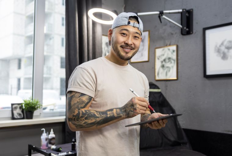 A young male tattoo studio owner smiles as he sketches his latest tattoo designs.