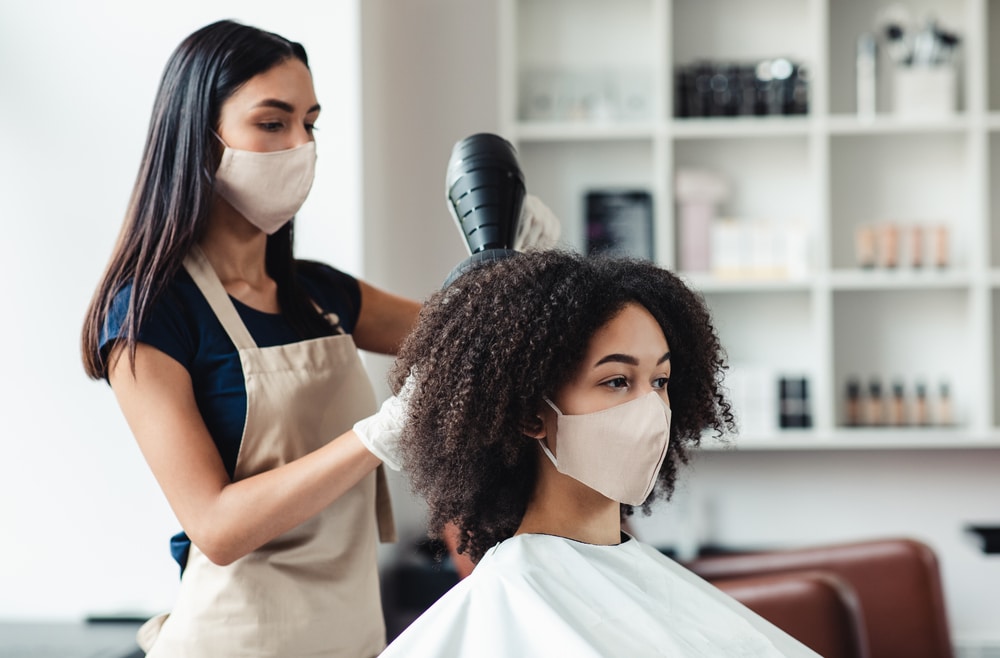 Stylist blow drying someone's hair at a salon.