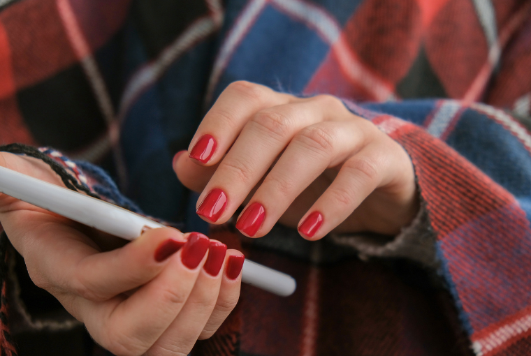 Close up of hands with shiny red nails holding a white mobile phone