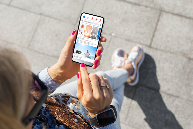 A trendy looking woman holds a mobile in her manicured hand and scrolls on a social media platform