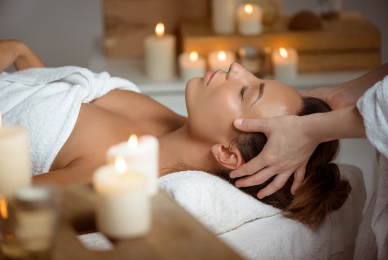 A woman lies on the massage table in an immaculate spa, surrounded by relaxing candles.