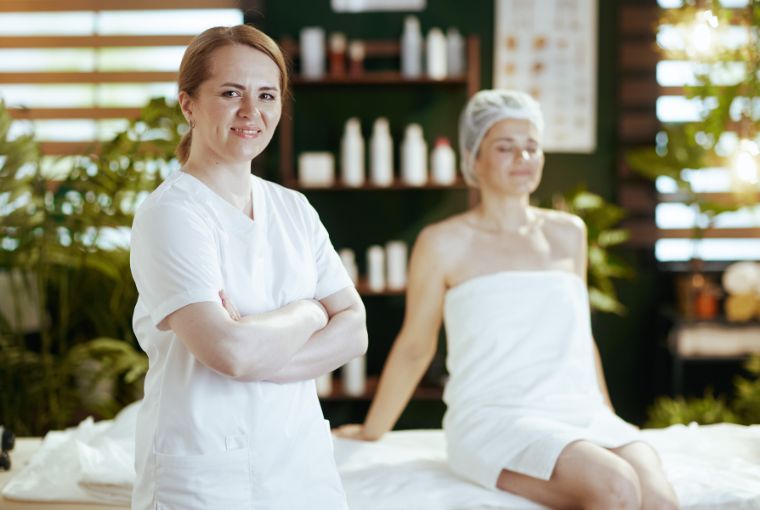 A confident spa professional looks at the camera as a happy client enjoys the results of a great massage.