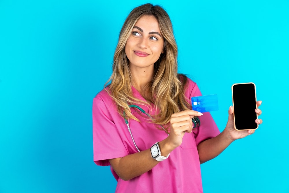 A female veterinary professional holds a credit card and a mobile phone to show different types of payment methods.