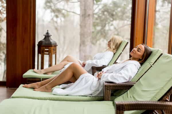 Two women in dressing gowns relaxing on reclining beds